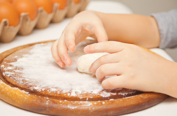 Little child in the home kitchen preparing dough for pizza or another food.