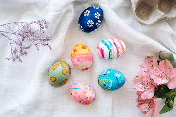 Happy easter Flat lay with Easter eggs painted in different colors on a white fabric with flowers for easter holiday celebration.