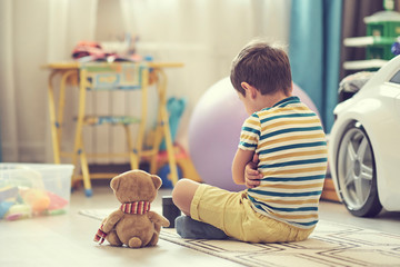sad boy sits on the floor of the nursery. lonely kid misses home
