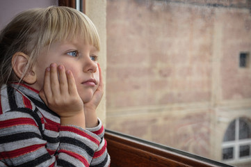 The white-haired blue-eyed girl looks out the window. Quarantined child. The child is sad at the...