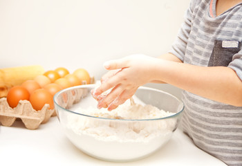 Little child in the home kitchen preparing dough for pizza or another food.