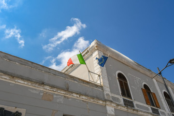 Fototapeta na wymiar An Italian flag and a torn European Union flag fly on top of a worn down building in Brindisi Italy in the Puglia region.