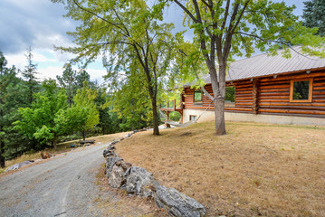 Fototapeta premium A rustic log cabin in a rural mountain setting with landscaped rocks and a hammock swing between two trees in the mountains of the USA.