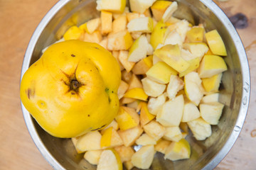 standing on a wooden chopping board . Quince fruit is cut into large pieces, composed in metallic heat resistant pot, bake,