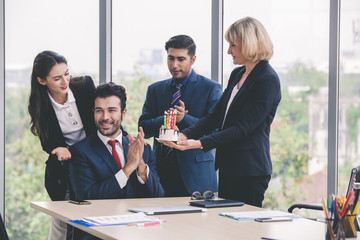 Business team celebrating male colleague's birthday with cake in office. Colleagues celebrating a birthday in the office