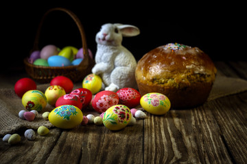Traditional holiday composition. Hand painting Easter eggs with orthodox sweet bread on a dark wooden table. With rabbit figure. Selective focus.