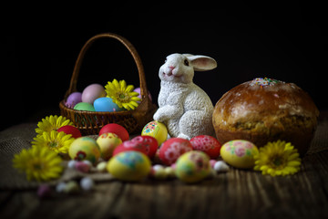 Traditional holiday composition. Hand painting Easter eggs with orthodox sweet bread on a dark wooden table. With rabbit figure. Selective focus. Close-up.