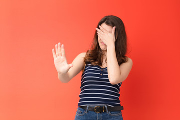 young pretty woman covering face with hand and putting other hand up front to stop camera, refusing...