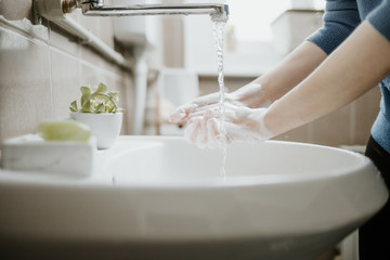 Closeup of a woman washing her hands in bathroom to prevent Covid-19 viral infection. Recommended washing with soap and running water during coronavirus pandemic.