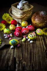 Traditional holiday composition. Hand painting Easter eggs with orthodox sweet bread on a dark wooden table. With rabbit figure. Selective focus.