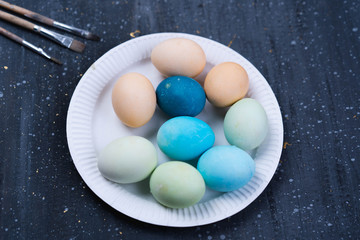 dark background, white dish, a lot of eggs on it, brushes for painting, holiday, Easter
