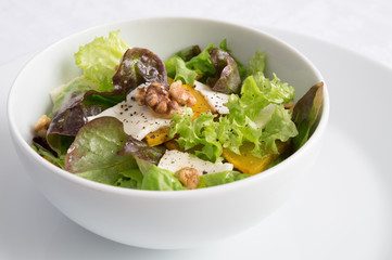 a bowl of leaf vegetables salad with roasted pumpkin and walnuts, and feta dressed with oil and vinegar
