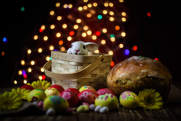 Traditional holiday composition. Hand painting Easter eggs with orthodox sweet bread on a dark wooden table. With rabbit figure. Selective focus.