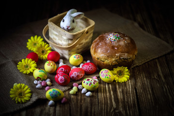 Traditional holiday composition. Hand painting Easter eggs with orthodox sweet bread on a dark wooden table. With rabbit figure. Selective focus. Close-up.