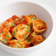 a bowl of ravioli with tomato sauce decorated with parsley 