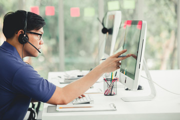 Young handsome male customer support phone operator with headset working in call center. Handsome male call center worker talking with a client and using computer in office