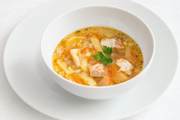 a bowl of salmon soup decorated with parsley leaves served on a plate 