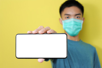 Young Asian man wearing protect mask showing smartphone with blank screen