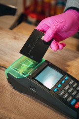 Woman in pink protective glove paying with contactless card at food store during quarantine. Closeup view of terminal and map