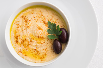 hummus sprinkled with paprika and olive oil decorated with olives and parsley 