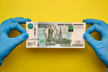 Hands in gloves hold money on a yellow background.