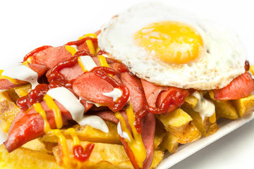 Peruvian street food:  Classic salchipapas or sausages and french fries  with ketchup, mustard, mayonnaise and chili peppers, decorated with a fried egg on the top and served on a white plate