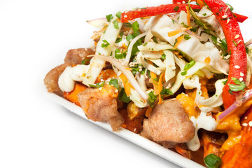 Peruvian street food:  Asian version of the salchipapas with pork rind and sweet potato fries  with chili peppers, decorated with veggies and sesam seeds on the top and served on a white plate