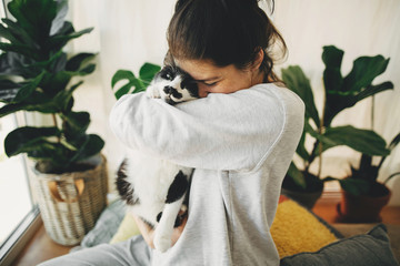 Happy hipster girl hugging cute cat, sitting together at home during coronavirus quarantine. Stay...