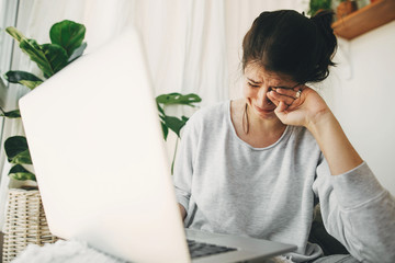 Young woman worries about losing job, depression. Unemployment and economic crisis. Financial instability. Sad girl crying from bad news, sitting with laptop home alone during quarantine. - obrazy, fototapety, plakaty