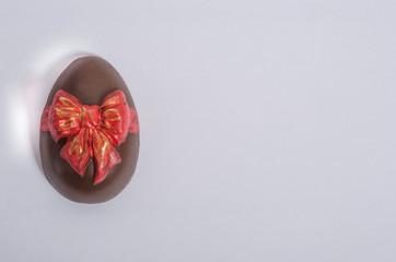 Chocolate easter egg with icing in the form of a red bow on a white background with copy space.