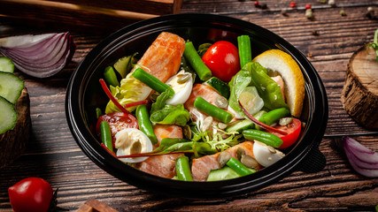 Balanced diet, keto diet. Seafood salad, salmon fish, green beans, quail eggs, lemon, tomato and cucumber. The concept of sports nutrition in disposable eco dishes.