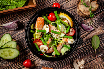 Balanced diet, keto diet. Seafood salad, salmon fish, green beans, quail eggs, lemon, tomato and cucumber. The concept of sports nutrition in disposable eco dishes.