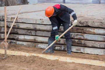 Preparation of sand base for concrete slab. Manual labor at a construction site. Work with a hand tool. A man throws sand with a shovel