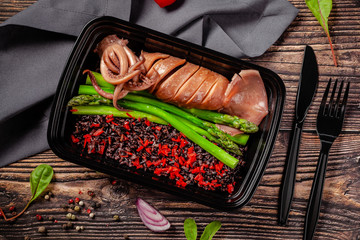 Balanced diet, keto diet. Seafood squid and octopus with black rice, paprika and asparagus. The concept of sports nutrition in disposable eco dishes.