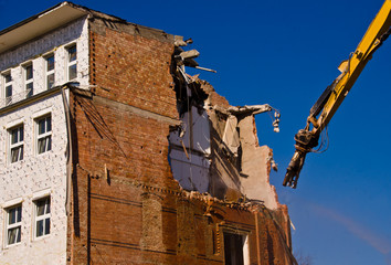 A demolition of a building with a crane with a blue sky background