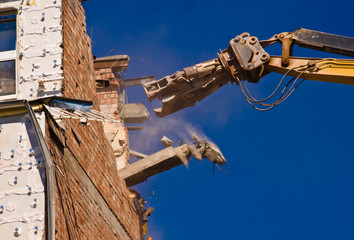 A demolition of a building with a crane with a blue sky background