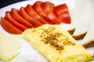 Amazing breakfast with tasty omelet, tomatoes, cheese, bread and sauce on the white plate. Delicious omelet made like rolle, other ingredients. Tasty and diet food. Healthy meal for breakfast or lunch