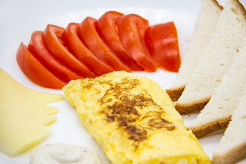Amazing breakfast with tasty omelet, tomatoes, cheese, bread and sauce on the white plate. Delicious omelet made like rolle, other ingredients. Tasty and diet food. Healthy meal for breakfast or lunch