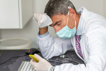 Fototapeta na wymiar Tired doctor wearing mask and gloves at the hospital in coronavirus times, checking his smartphone