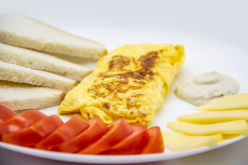 Amazing breakfast with tasty omelet, tomatoes, cheese, bread and sauce on the white plate. Delicious omelet made like rolle, other ingredients. Tasty and diet food. Healthy meal for breakfast or lunch