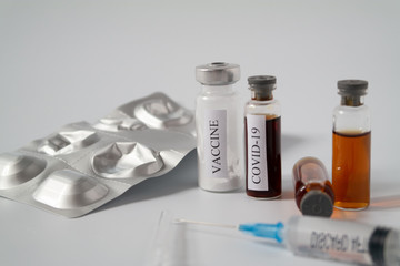 A package of tablets, a medical syringe and test tubes with a liquid labeled COVID-19 and a powder labeled vaccine. Concept of vaccination and medicine for a disease, virus test and an antiviral drug.