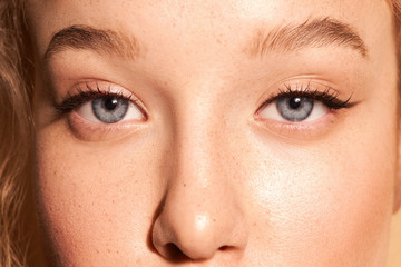 Close-up face of a young girl. Fresh make-up. Clean skin. Curly hair. Arrows on the eyes. Blue eyes. Natural retouching