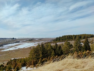 spring landscape on a hillside with views of fields and trees against a blue sky with clouds