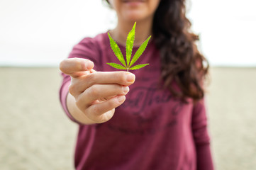 Crop woman showing cannabis leaf on beach