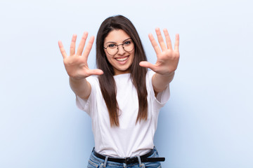 young pretty woman smiling and looking friendly, showing number ten or tenth with hand forward,...