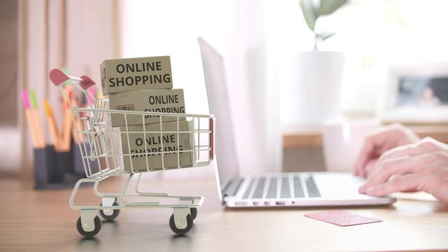 Boxes with ONLINE SHOPPING text fall in shopping cart right after placing order by customer on the laptop. Conceptual video with 3D animation