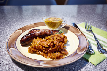 The grilled sausages with sauerkraut and mustard sauce lies on a plate, Tableware, Fork, knife, napkins
