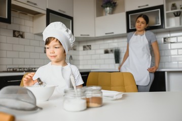 Child helping mother make cookies in modern kitchen