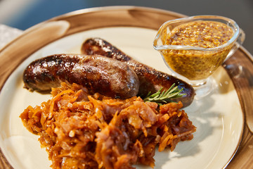 The grilled sausages with sauerkraut and mustard sauce lies on a plate, Tableware, Fork, knife, napkins