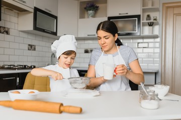 Young mother and her little son baking cookies together at home kitchen